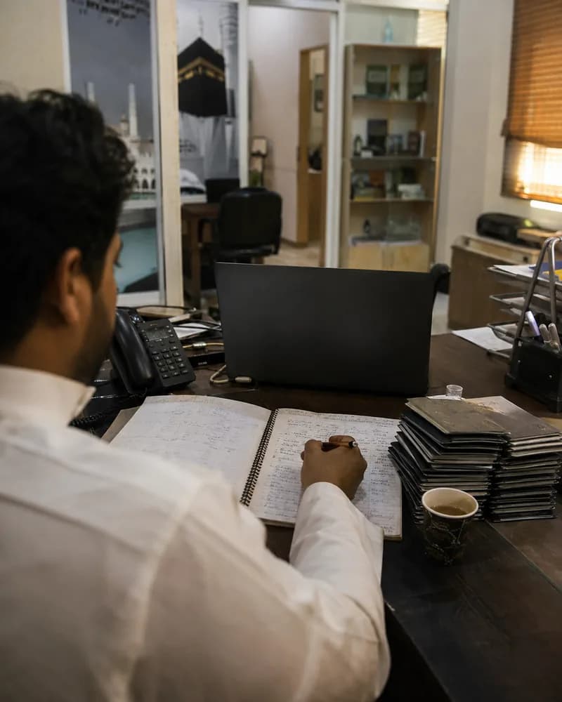 An Umrah booking agent working at a desk in a small travel agency
